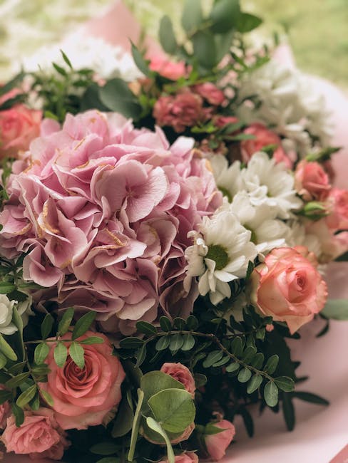 A close-up of a fresh floral bouquet featuring soft pink hydrangeas with large, ruffled petals, complemented by delicate pale pink roses with tightly layered petals, and white daisies with yellow cent