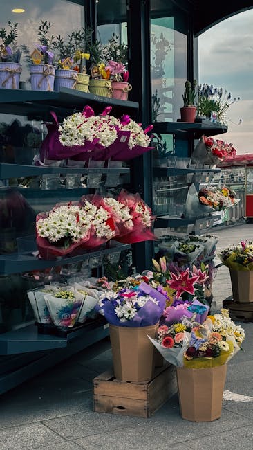 A variety of floral arrangements and bouquets displayed outdoors at Brent Cross Shopping Centre, showcasing fresh flowers in vibrant colors such as white, pink, purple, and yellow. The flowers include